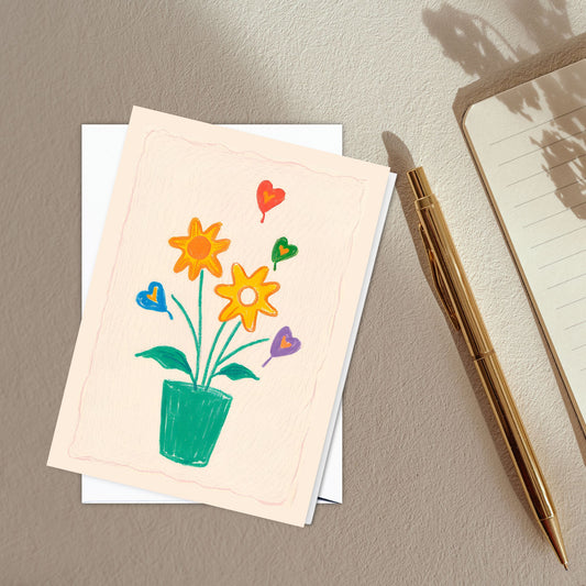 Folded Greeting Card featuring a minimalist, yet whimsical and vibrant colored pencil design boasting a vase adorned with flowers and hearts in green, yellow, orange and blue hues, set against a serene antique white backdrop. 